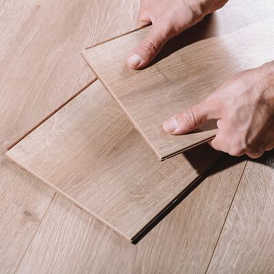 Zwei Hände halten prüfend einen hellbraunen Vinylboden fest und kontrollieren die Beschaffenheit des Designbodens