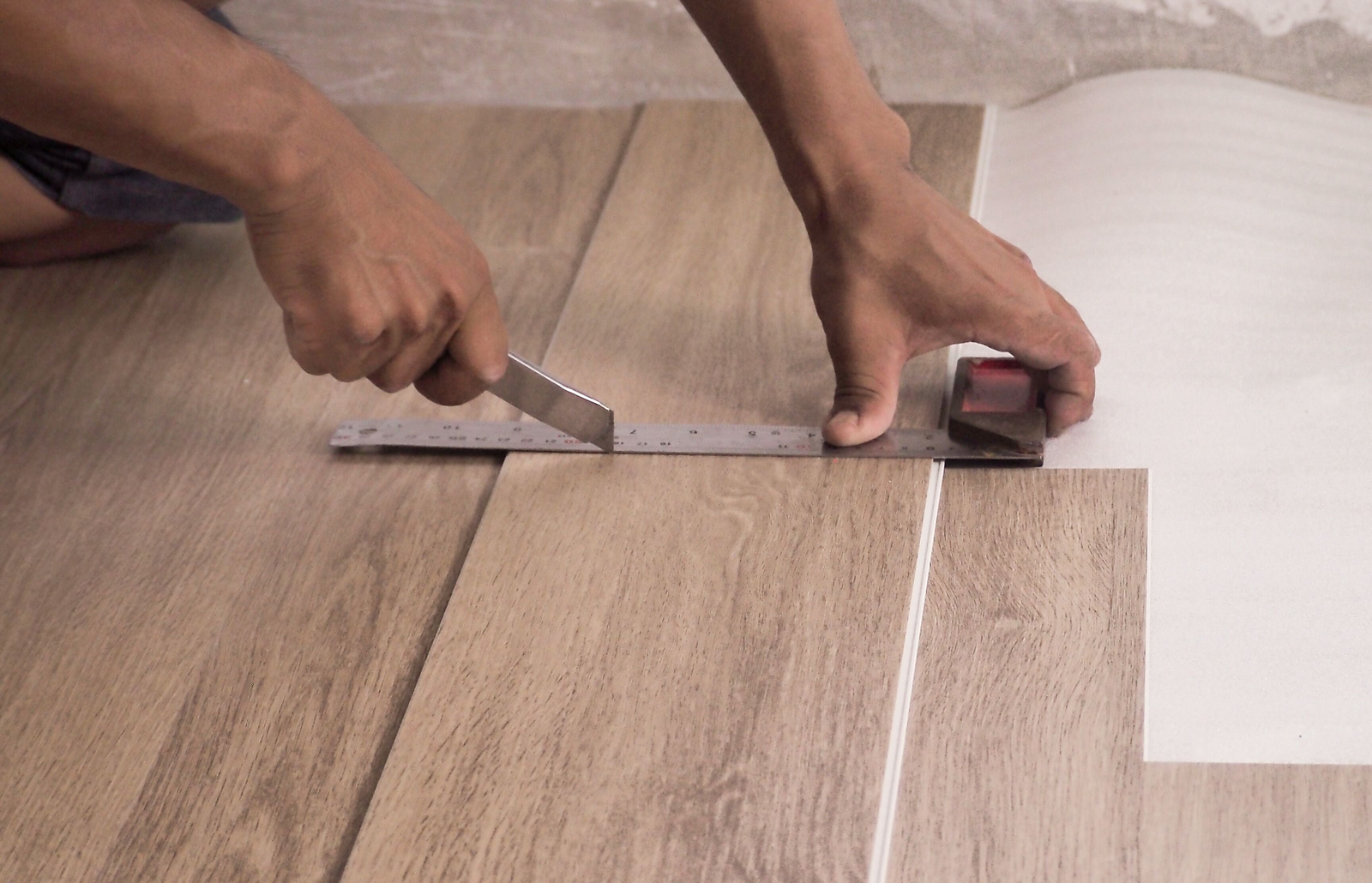 Ein Fußbodenmonteur ritzt mit einem Cuttermesser eine Vinylbodendiele ein