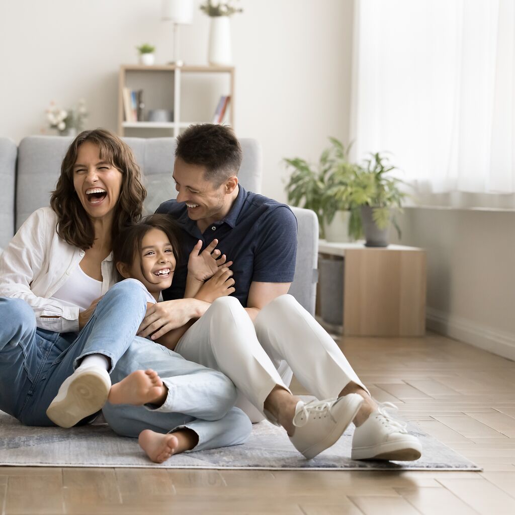 Eine glückliche, lachende Familie aus München sitzt auf einem Teppich, der auf einem hochwertigen Vinylboden liegt