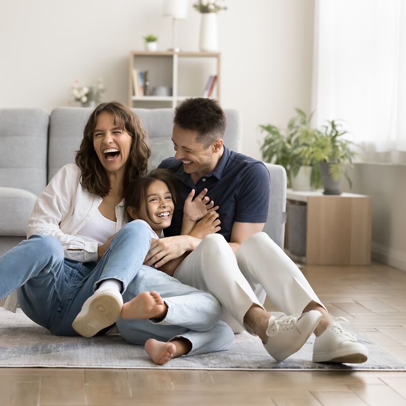 Eine lachende Familie aus Berlin sitzt auf einem Teppich, der auf einem hochwertigen Vinylboden liegt