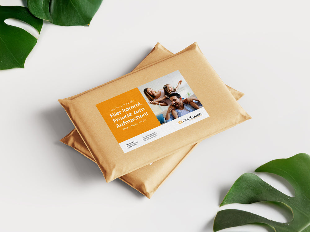 Zwei fertig verpackte Musterpakete liegen versandbereit auf einer hellen Oberfläche, umrahmt von grünen Blättern