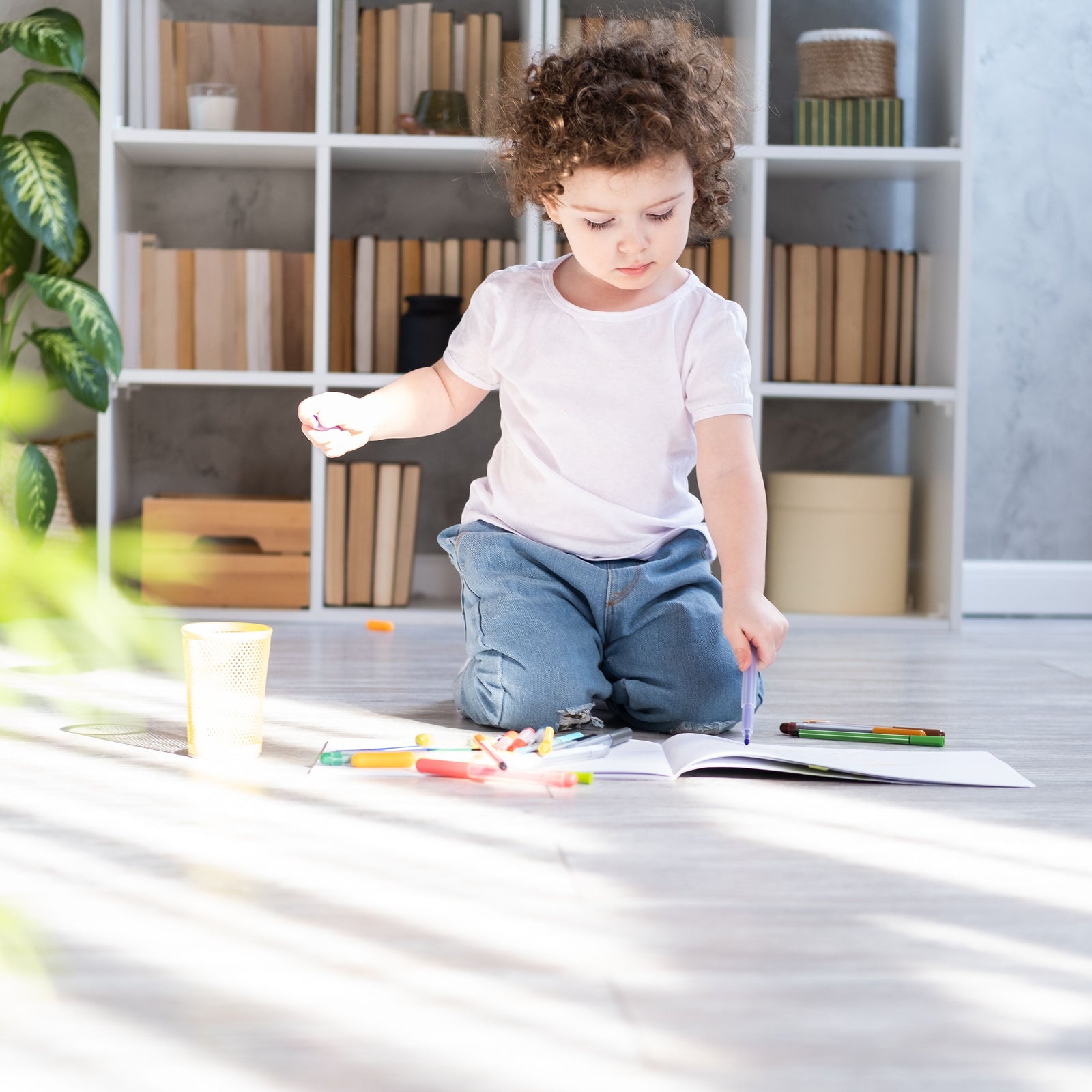 Ein kleines Mädchen sitzt auf einem umweltfreundlichen Vinylboden und malt konzentriert mit einem Stift in einem Malbuch