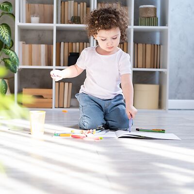 Ein kleines Mädchen sitzt auf einem umweltfreundlichen Vinylboden und malt konzentriert mit einem Stift in einem Malbuch