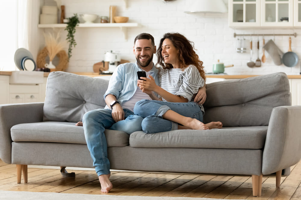 Ein glückliches Pärchen sitzt auf der Couch und freut sich über die 5% Rabatt, die sie bei der WhatsApp Newsletteranmeldung bekommen haben